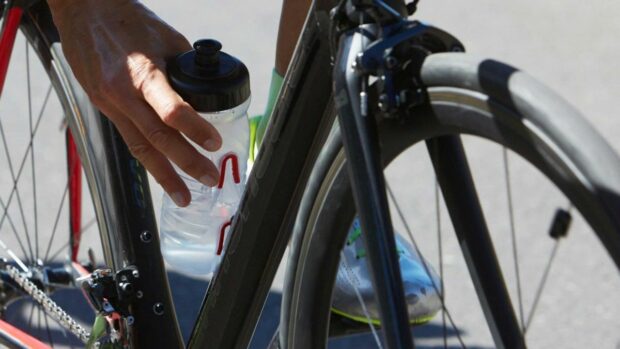A hand reaching down to a Fabric cageless water bottle, the rider about to drink mid-ride