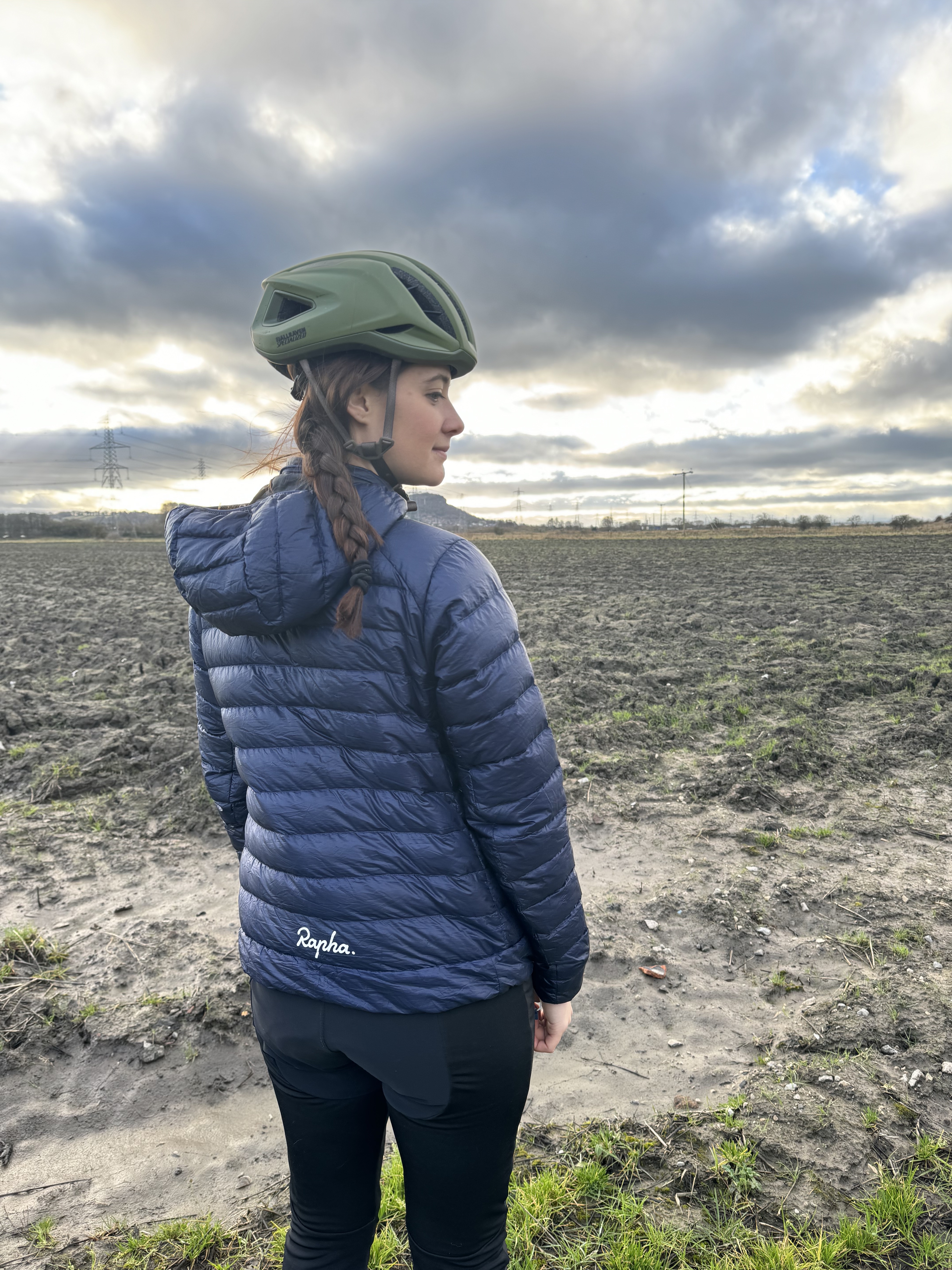 Une femme regarde loin de la caméra vers un champ boueux.  La veste est bleu marine.