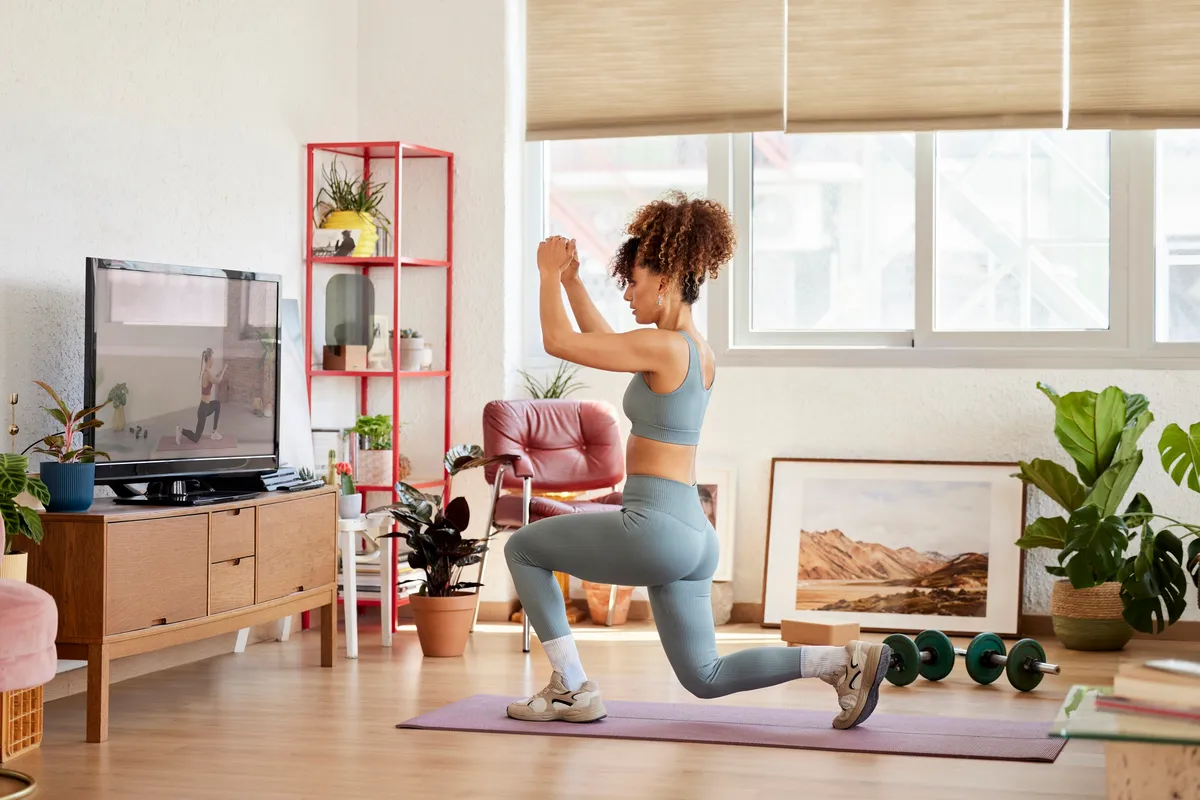 Toute la longueur d'une jeune femme apprenant des fentes tout en regardant un cours de yoga en ligne.  Une femme pratique de l'exercice à la maison.  Elle est dans le salon.