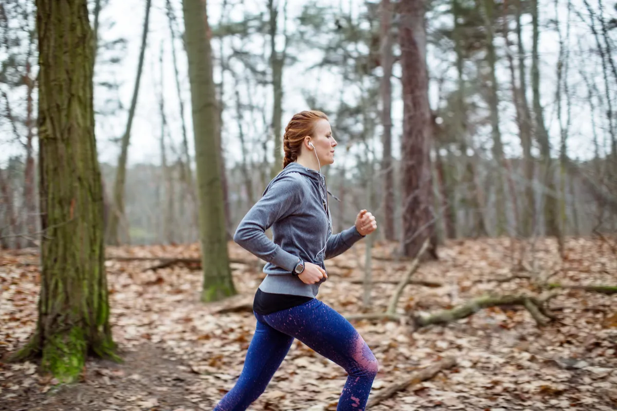 Vue latérale d'une femme déterminée faisant du jogging en forêt.