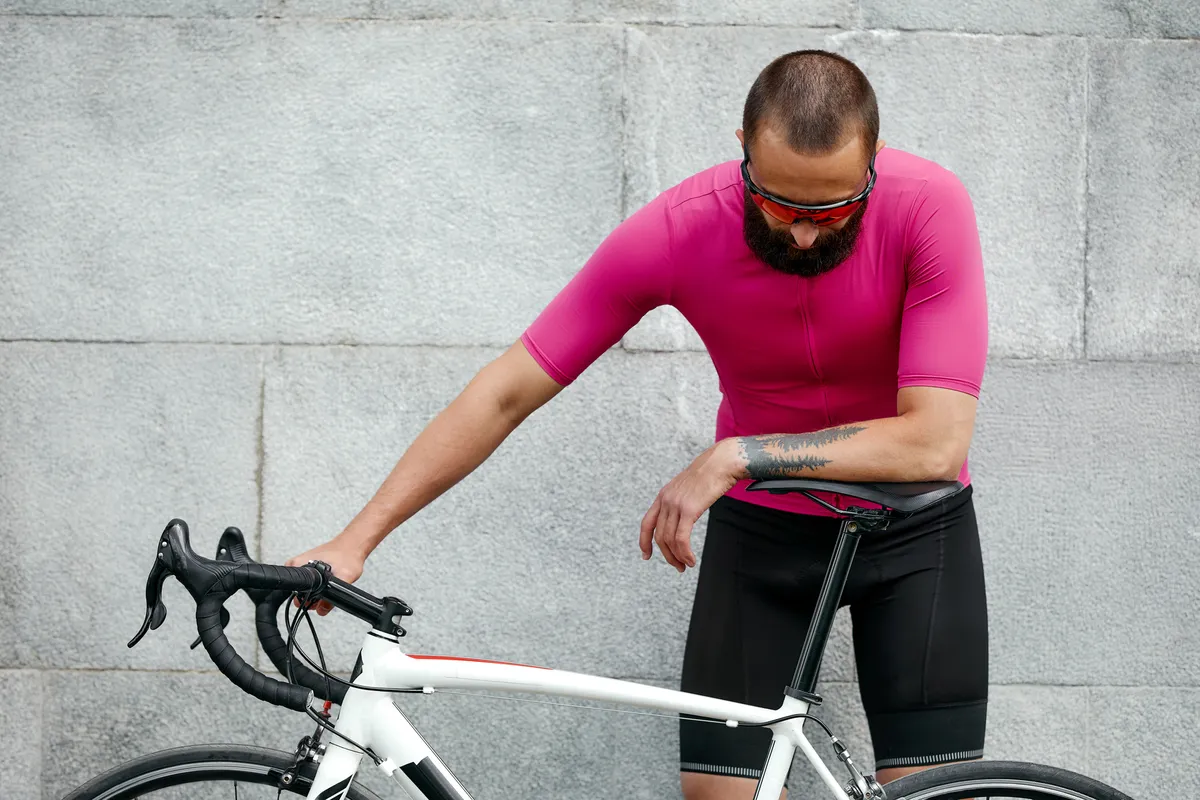 Cycliste en vêtements de sport roses se reposant après une séance d'entraînement debout contre un mur de ciment 