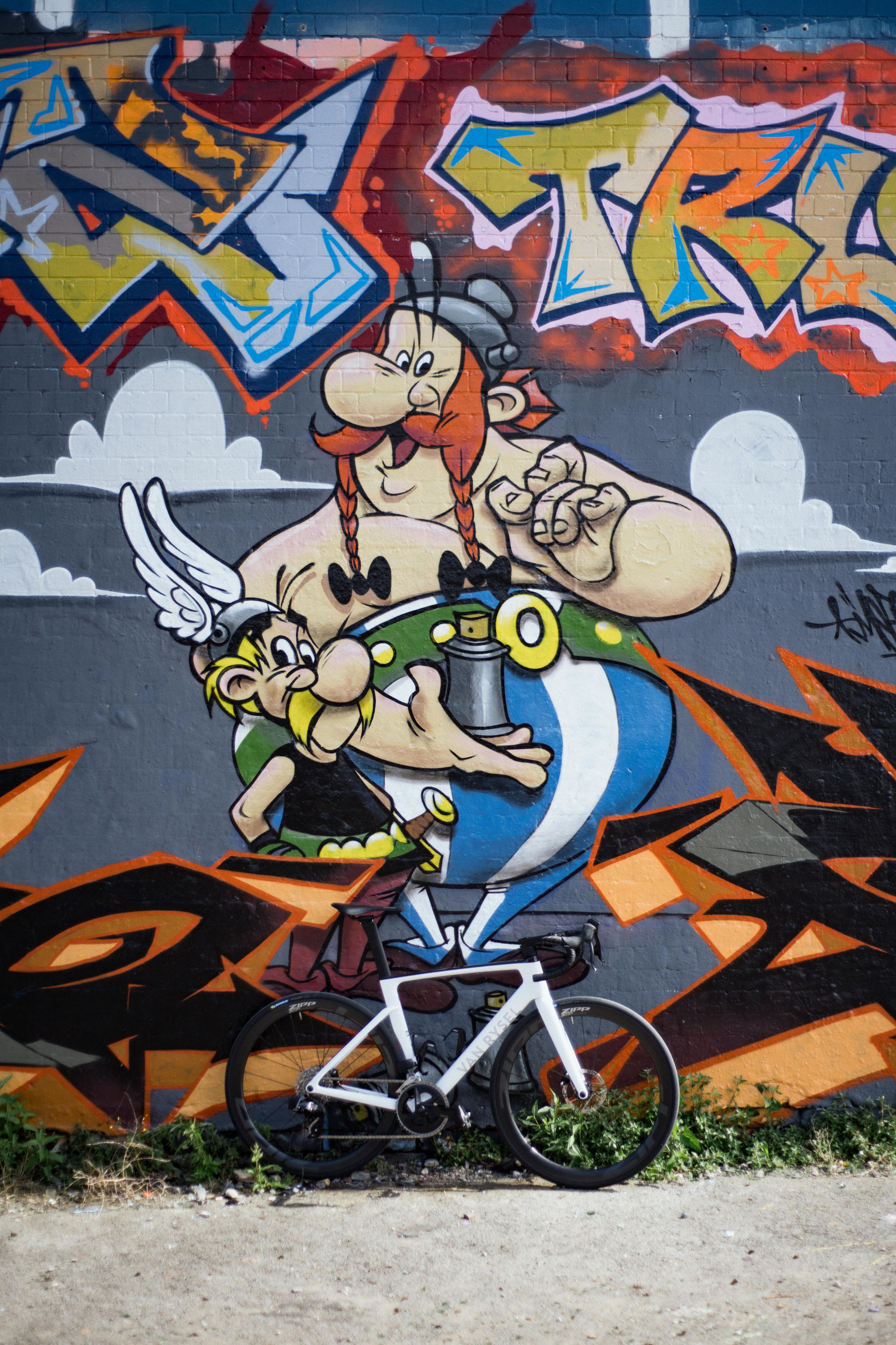 Un vélo blanc devant une fresque murale représentant Astérix et Obélix