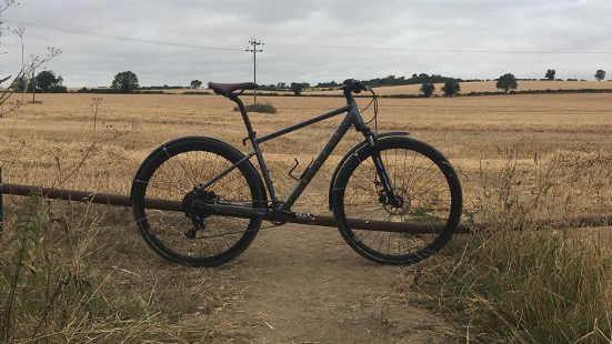 Une photo du Ribble Hybrid Trail AL dans un cadre rural avec un champ en arrière-plan