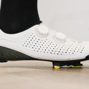 A close up of a white cycling shoe with a black socked foot in it