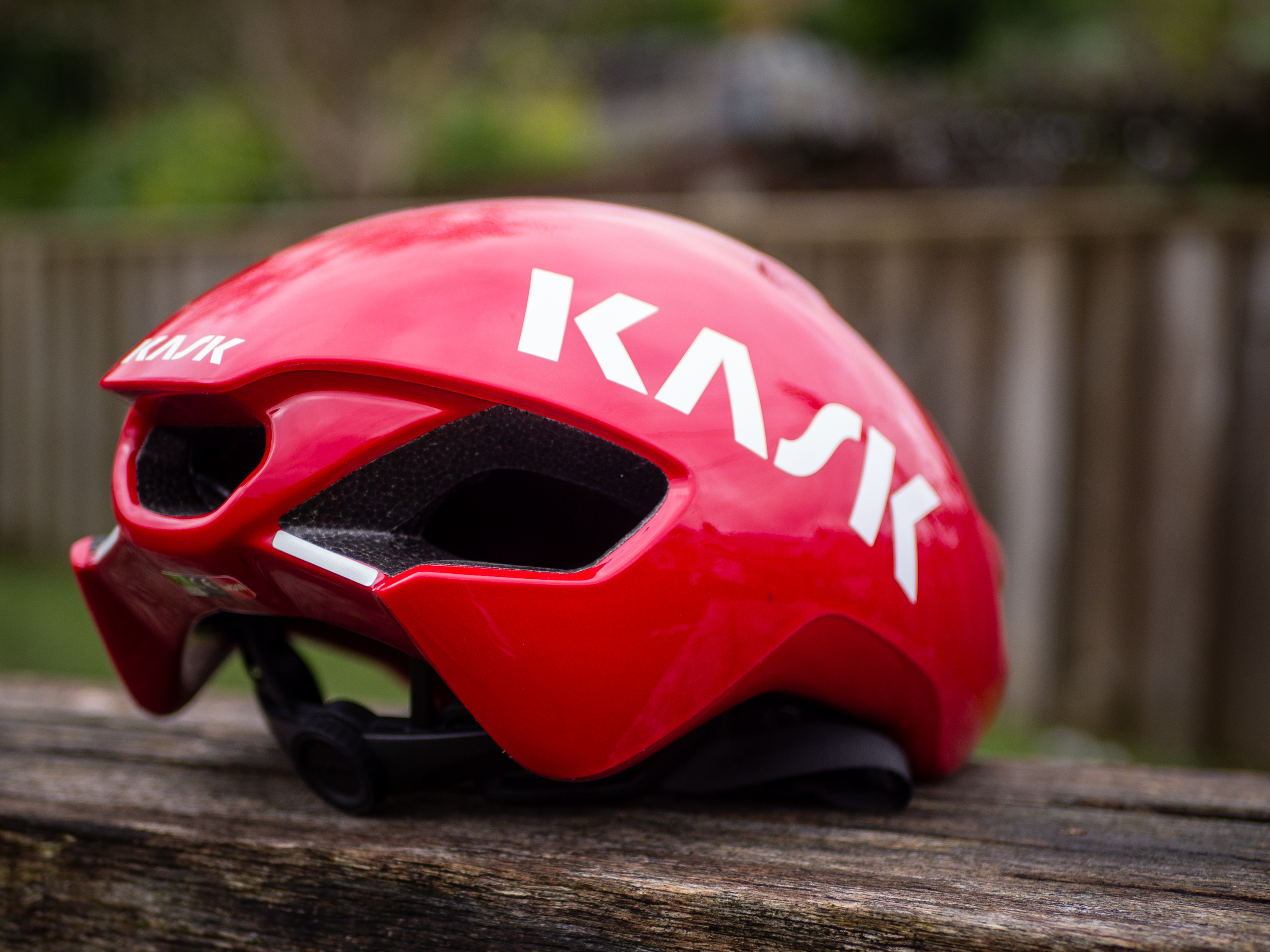 Un casque aérodynamique Kask Utopia Y rouge est posé sur un banc en bois