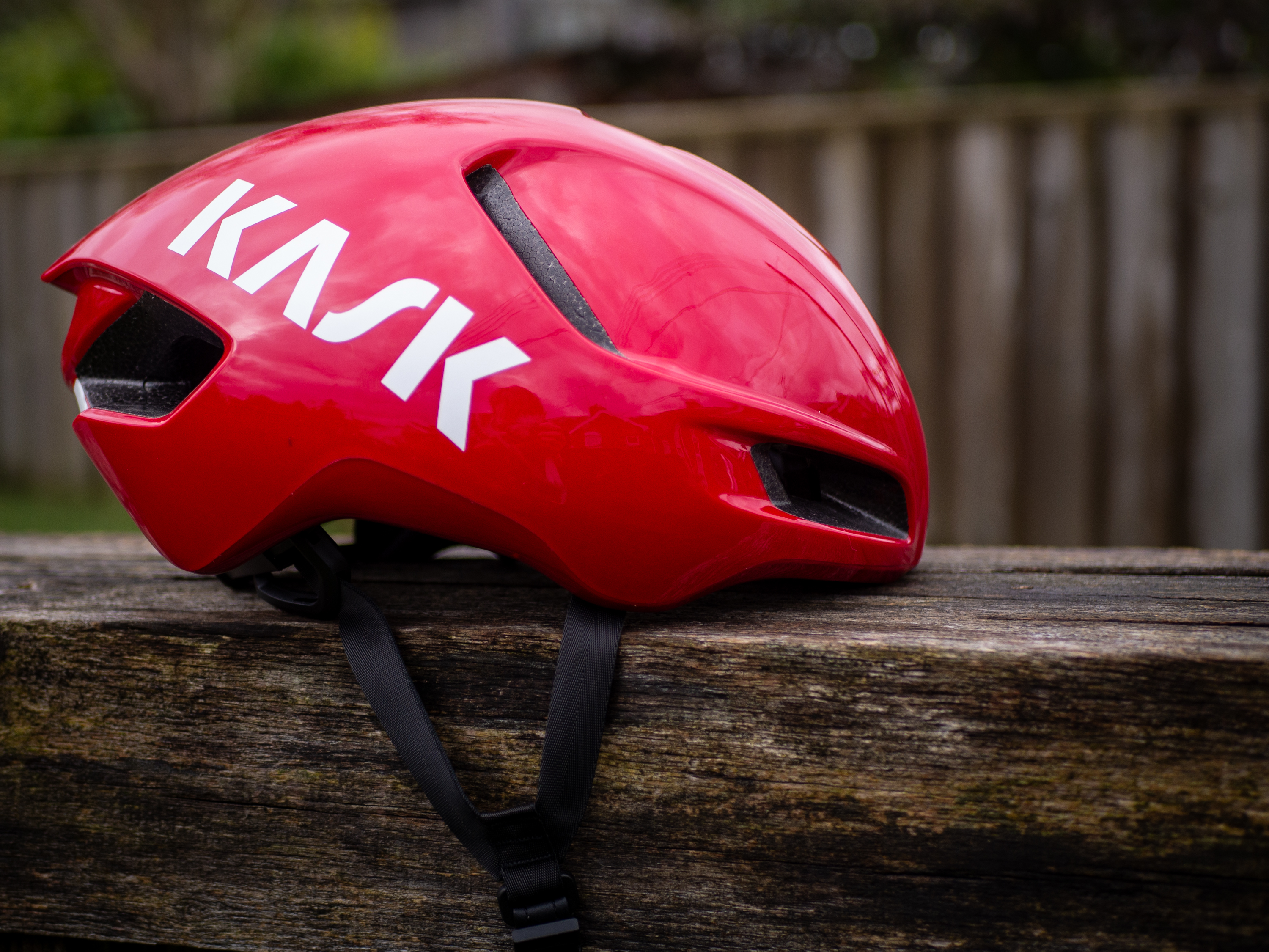 Un casque aérodynamique Kask Utopia Y rouge est posé sur un banc en bois