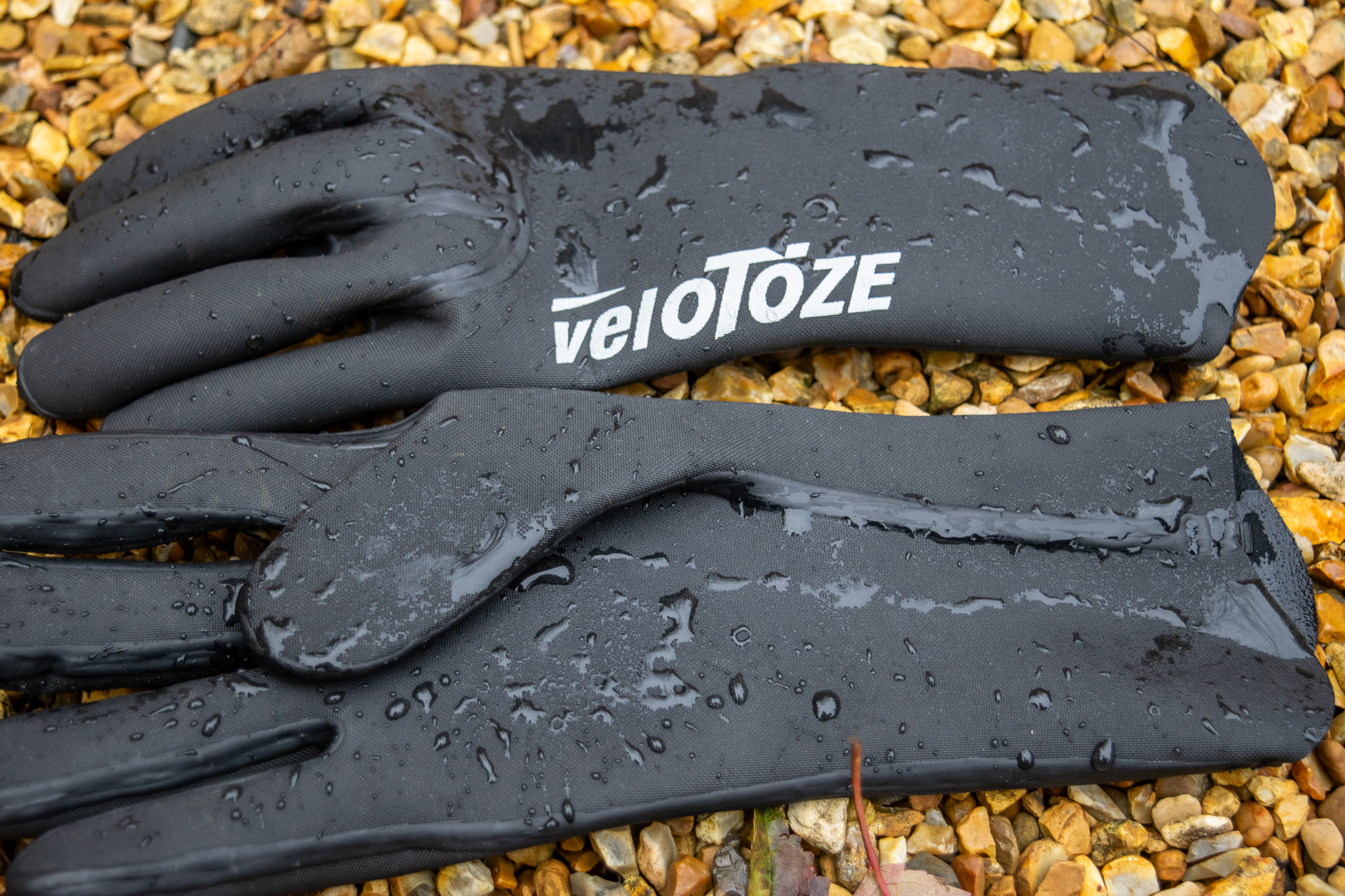 Gants en néoprène Velotoze sur du gravier avec des gouttelettes d'eau dessus