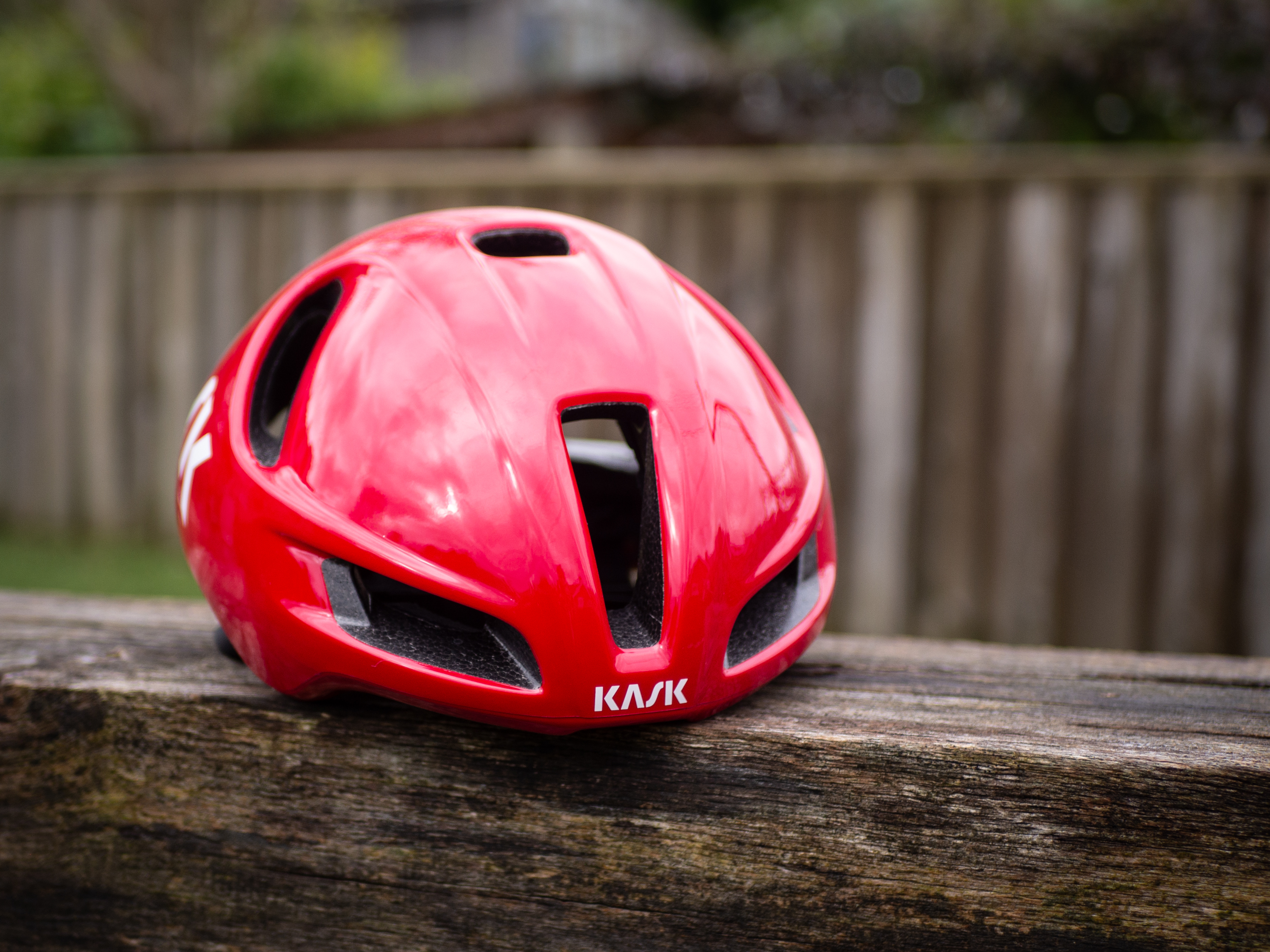 Un casque aérodynamique Kask Utopia Y rouge est posé sur un banc en bois