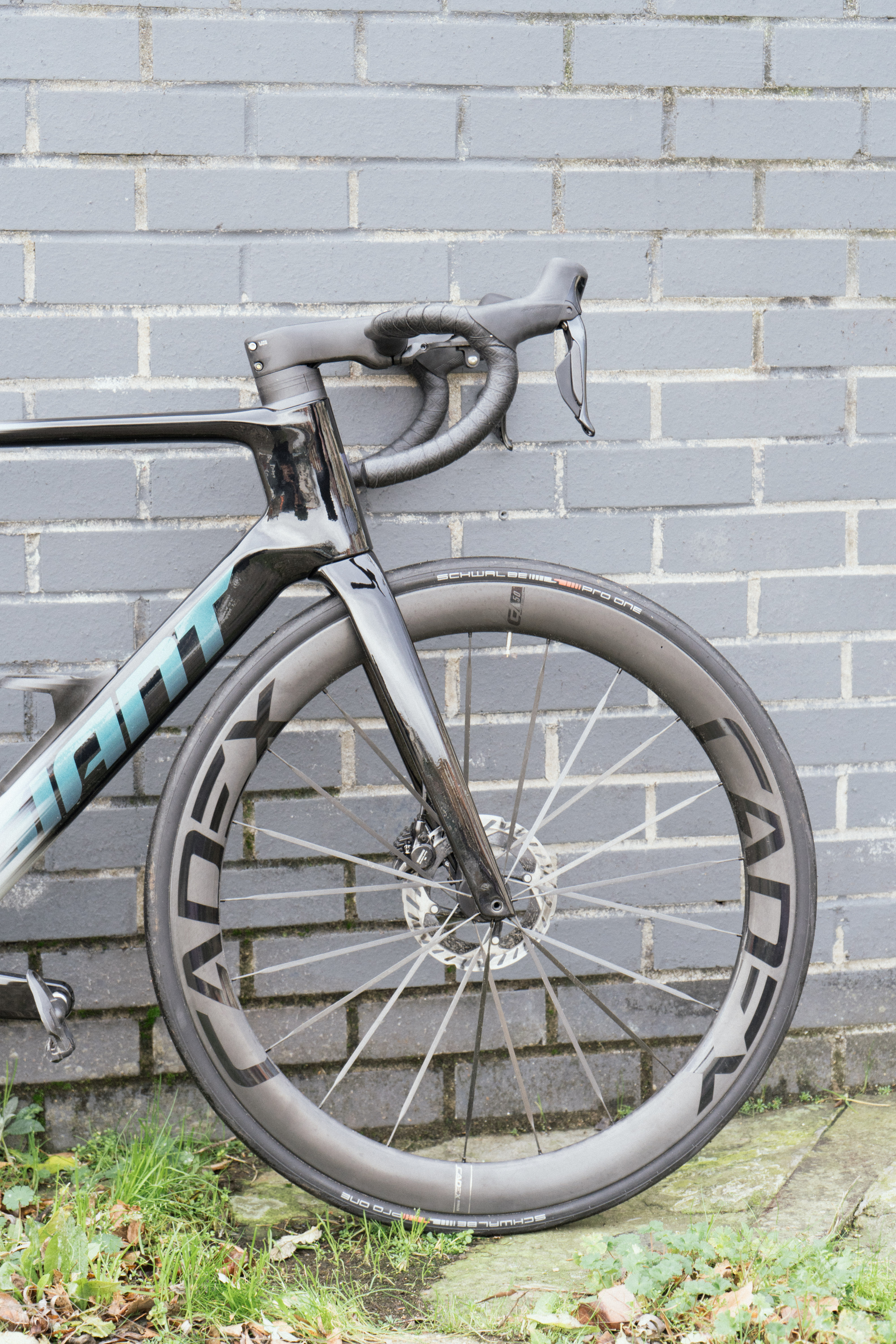 Un vélo noir avec des roues d'un noir profond contre un mur de briques gris foncé.