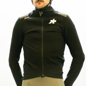 Will stands against a white wall while wearing the black Assos Johdah cycling jacket