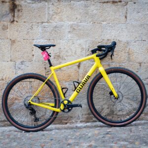 A yellow Guava Spot gravel bike leans against a wall